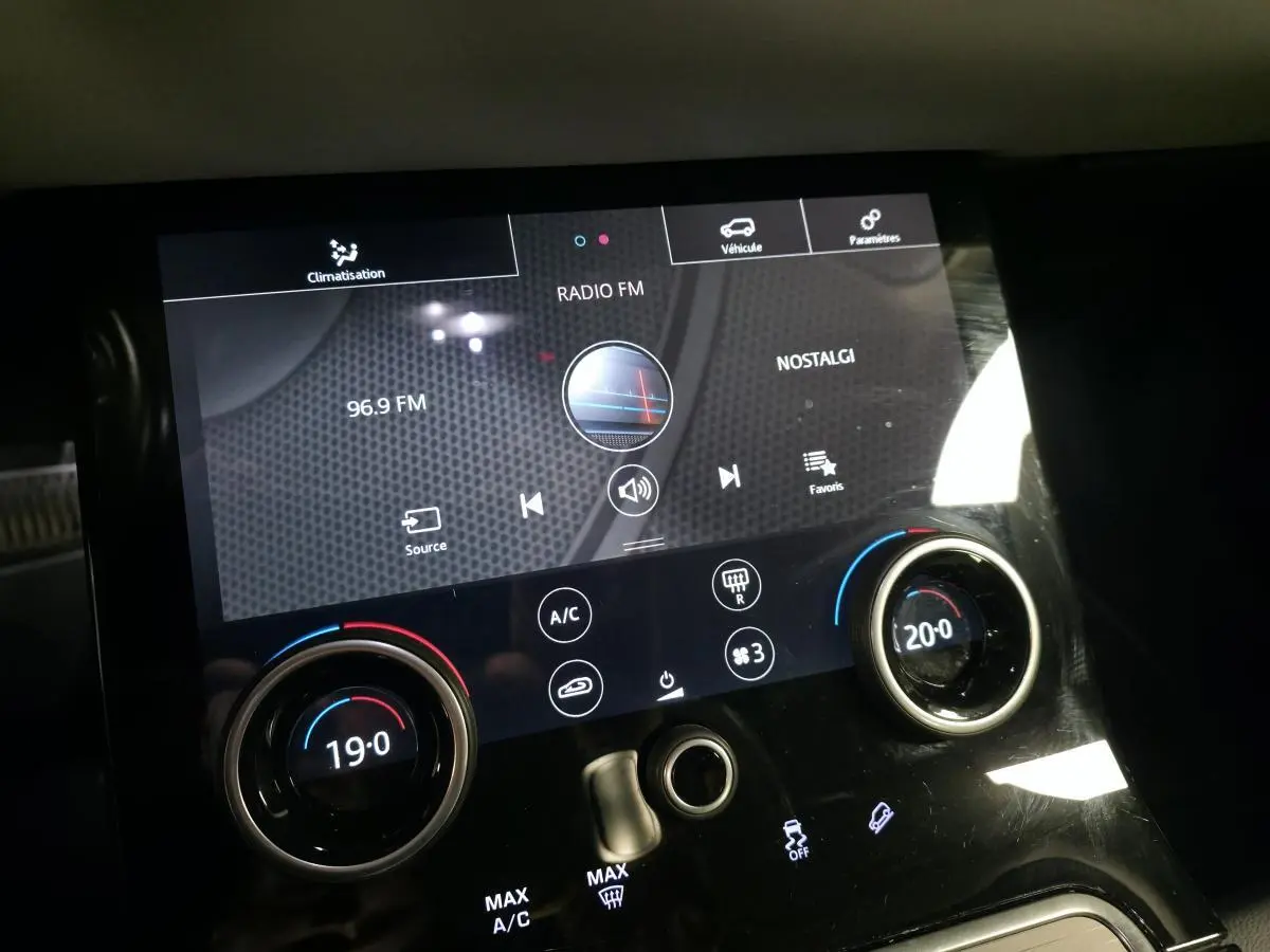 Gros plan sur la console centrale tactile du Range Rover Evoque rouge, affichant la radio et la climatisation bi-zone.