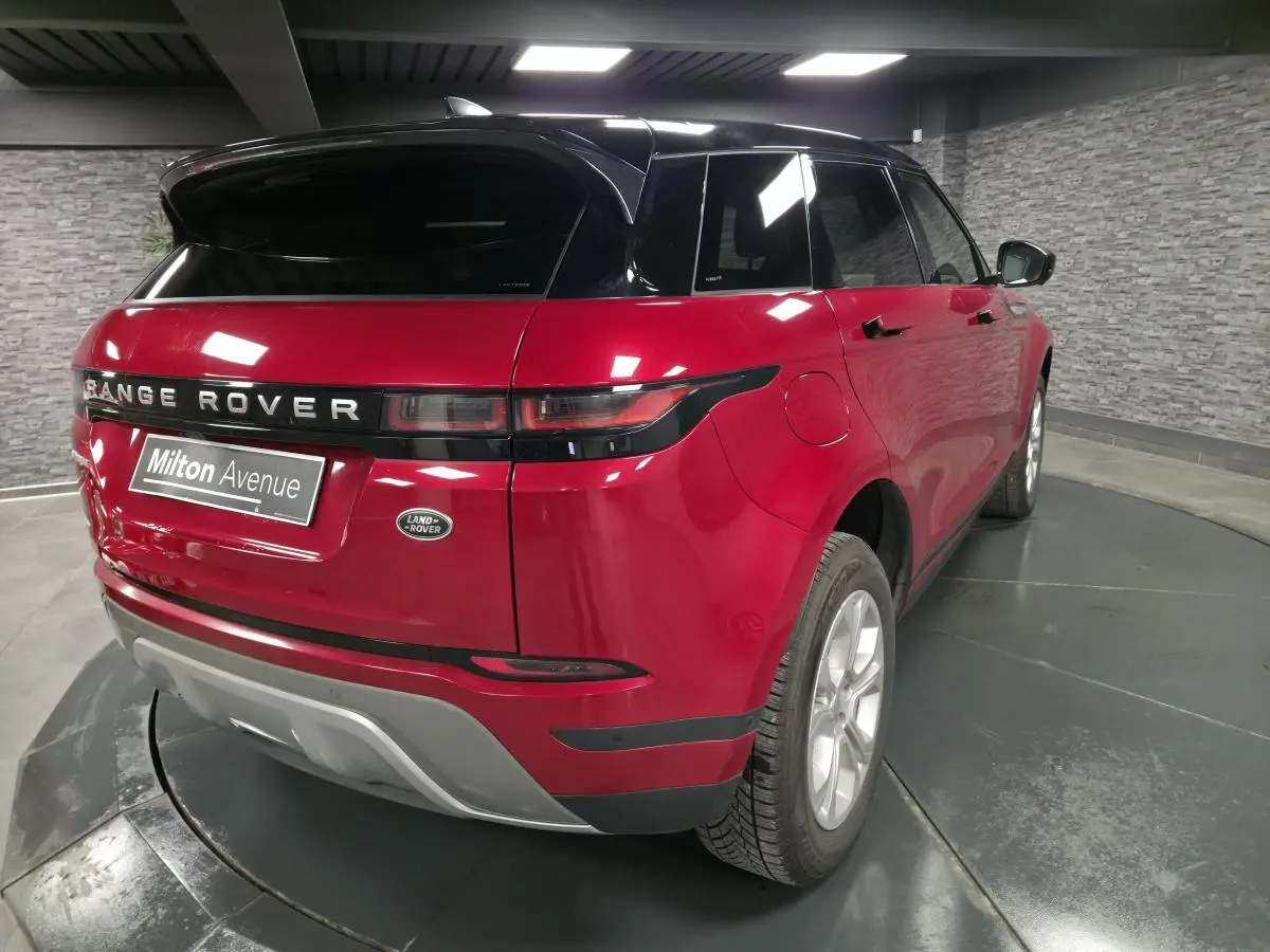 Vue 3/4 arrière droite d'un Range Rover Evoque rouge avec toit noir et feux arrière étirés en intérieur showroom.