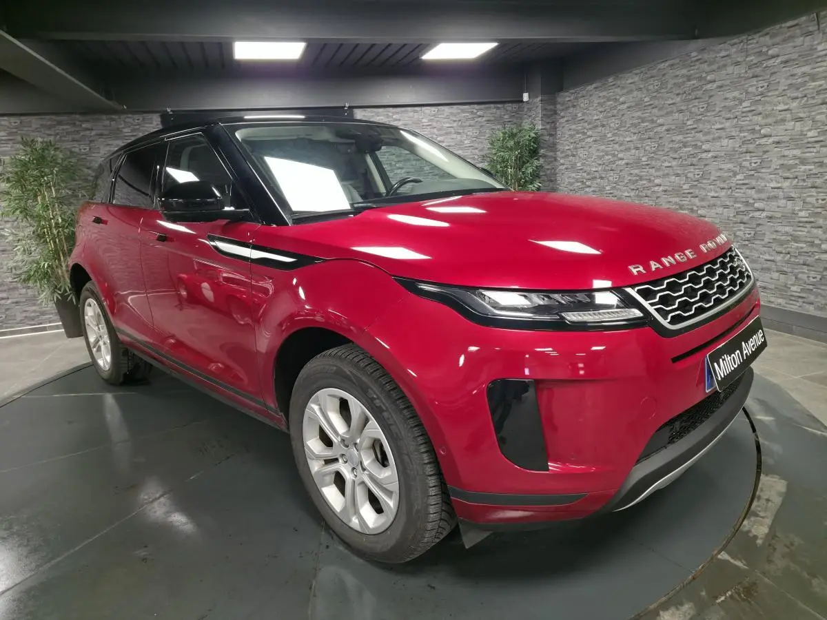 Range Rover Evoque rouge vue 3/4 avant droit avec toit noir et calandre distinctive en intérieur showroom.