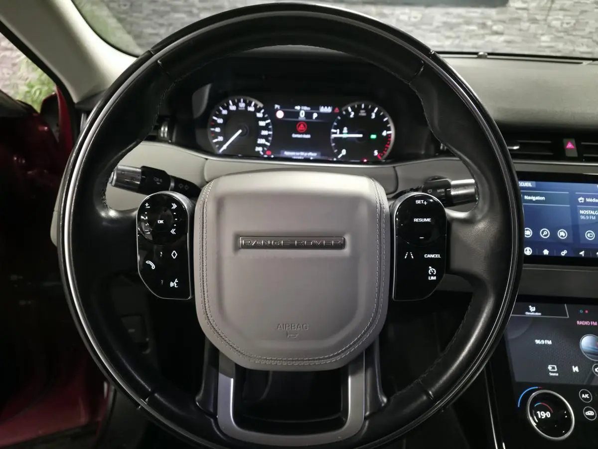 Vue rapprochée du volant cuir noir et gris avec logo Range Rover, tableau de bord et écran tactile du Range Rover Evoque rouge 2019.