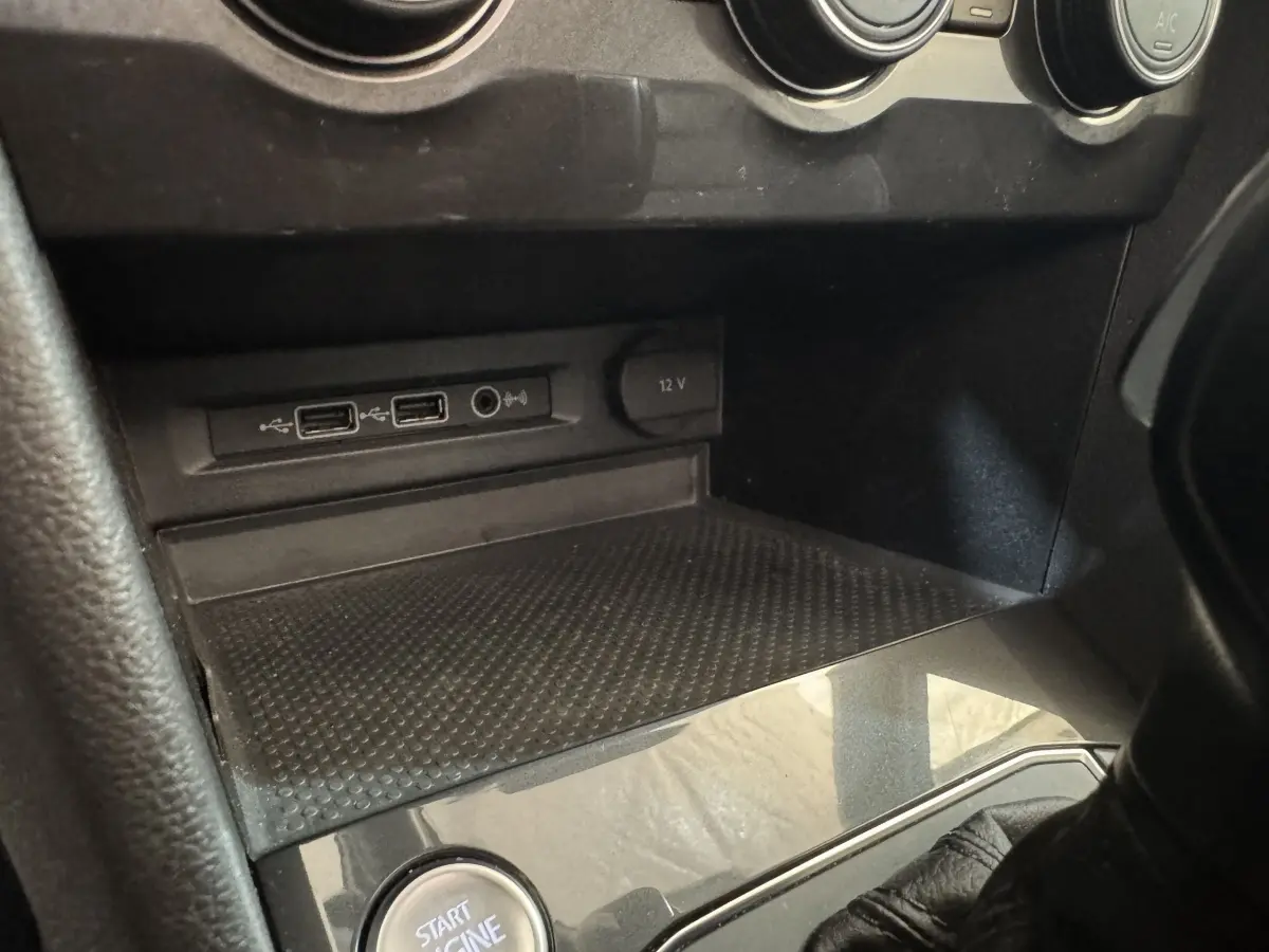 Gros plan sur la console centrale noire du Volkswagen Tiguan Allspace, montrant prises USB, prise 12V et bouton démarrage.