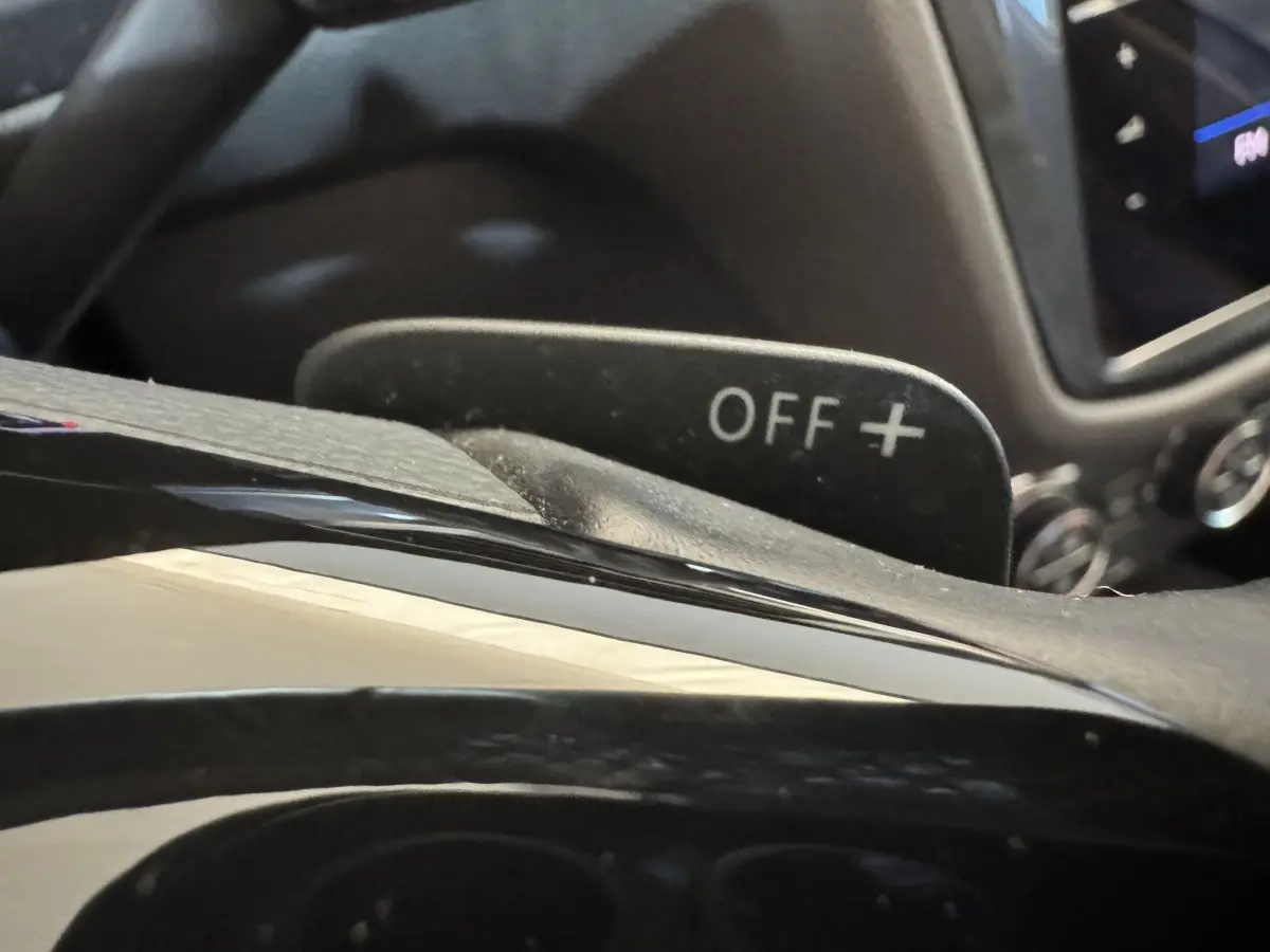 Gros plan sur la palette de changement de vitesse marquée "OFF +" dans l'habitacle du Volkswagen Tiguan Allspace gris foncé.