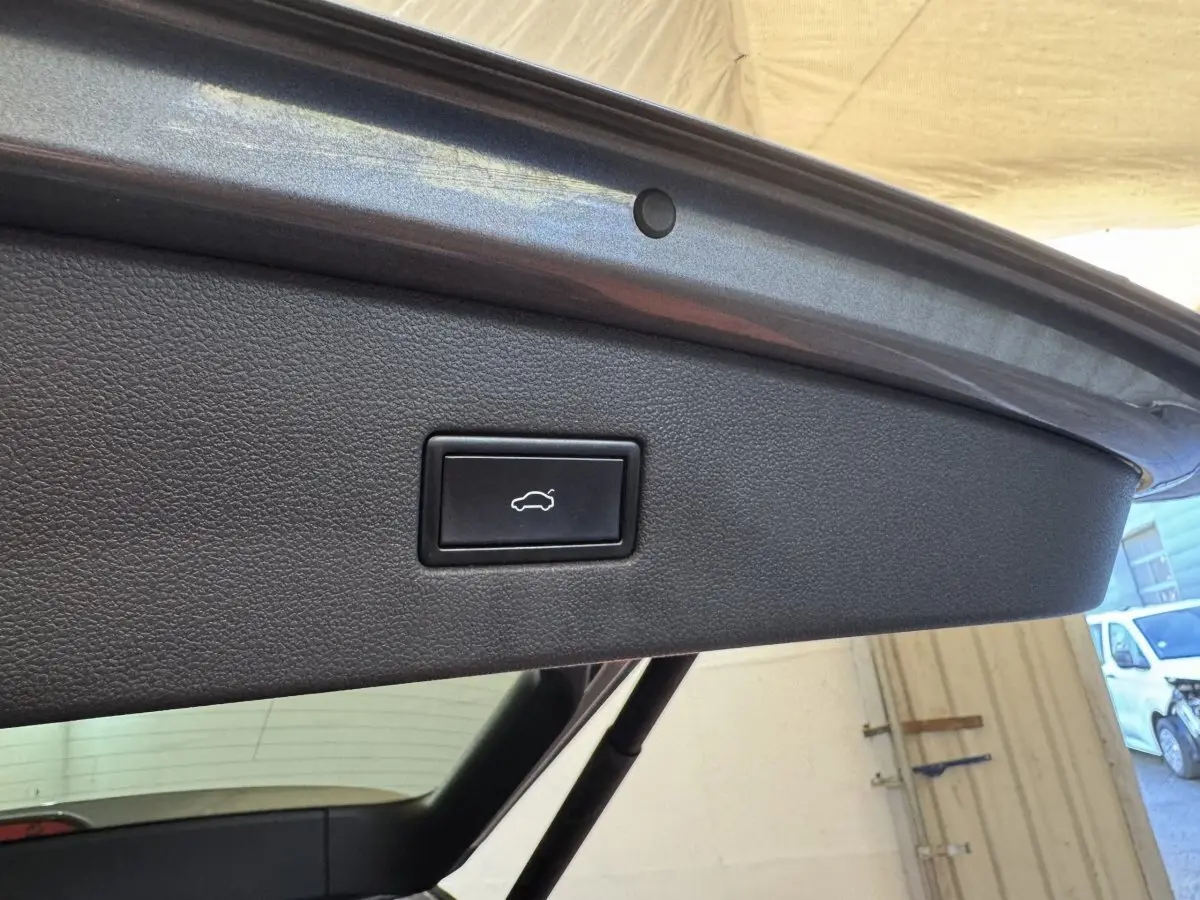 Gros plan sur le bouton d'ouverture électrique du coffre, situé sur le hayon intérieur gris foncé du Volkswagen Tiguan Allspace.