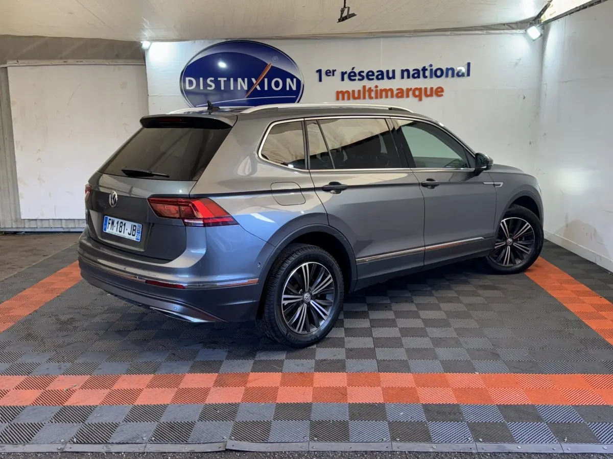 Vue 3/4 arrière droite d’un Volkswagen Tiguan Allspace gris foncé avec jantes alliage et vitres teintées en intérieur showroom.