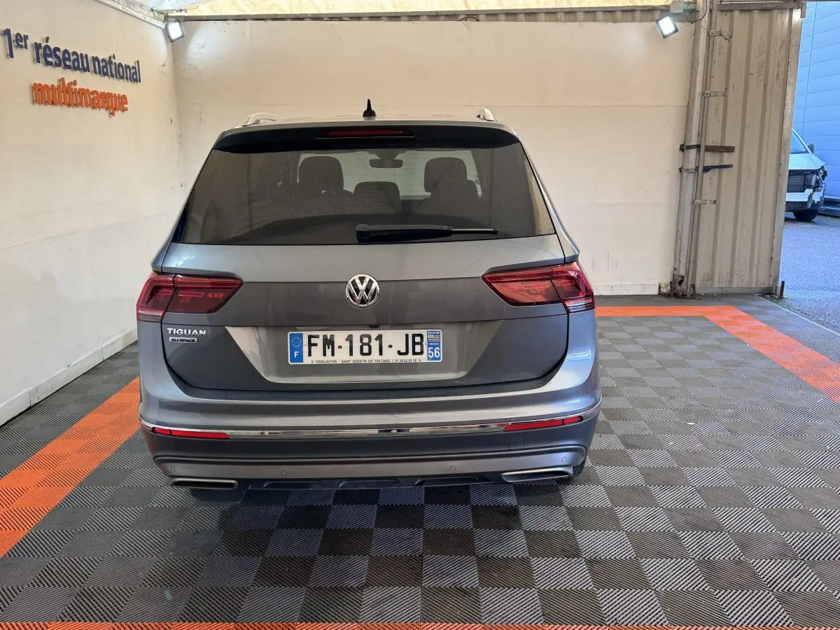 Vue arrière d'un Volkswagen Tiguan Allspace gris foncé stationné en intérieur sur un sol à damiers noir et orange.