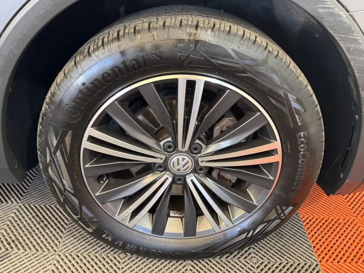 Gros plan sur la roue avant droite avec jante alliage noir et gris du Volkswagen Tiguan Allspace gris foncé.