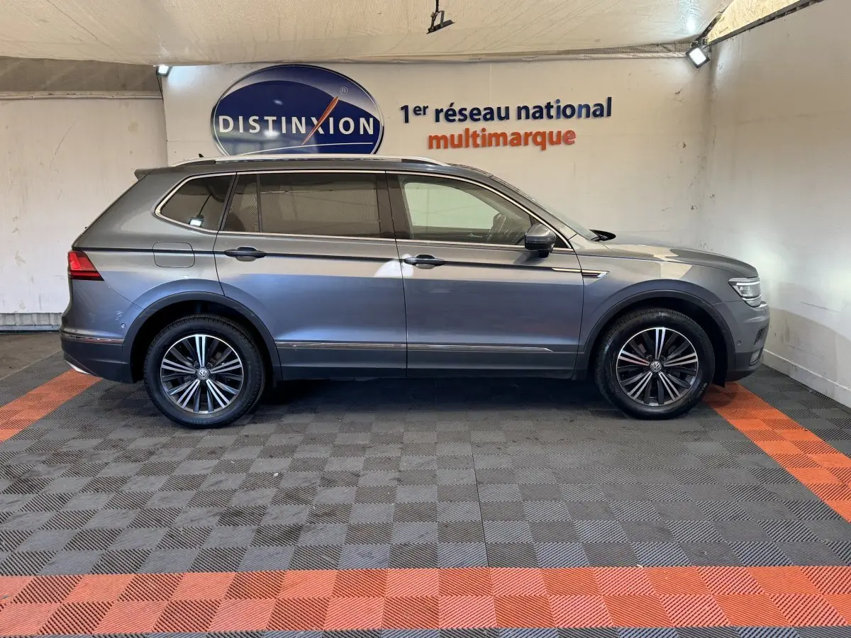Volkswagen Tiguan Allspace gris foncé vu de profil côté gauche dans un showroom avec jantes alliage noires.