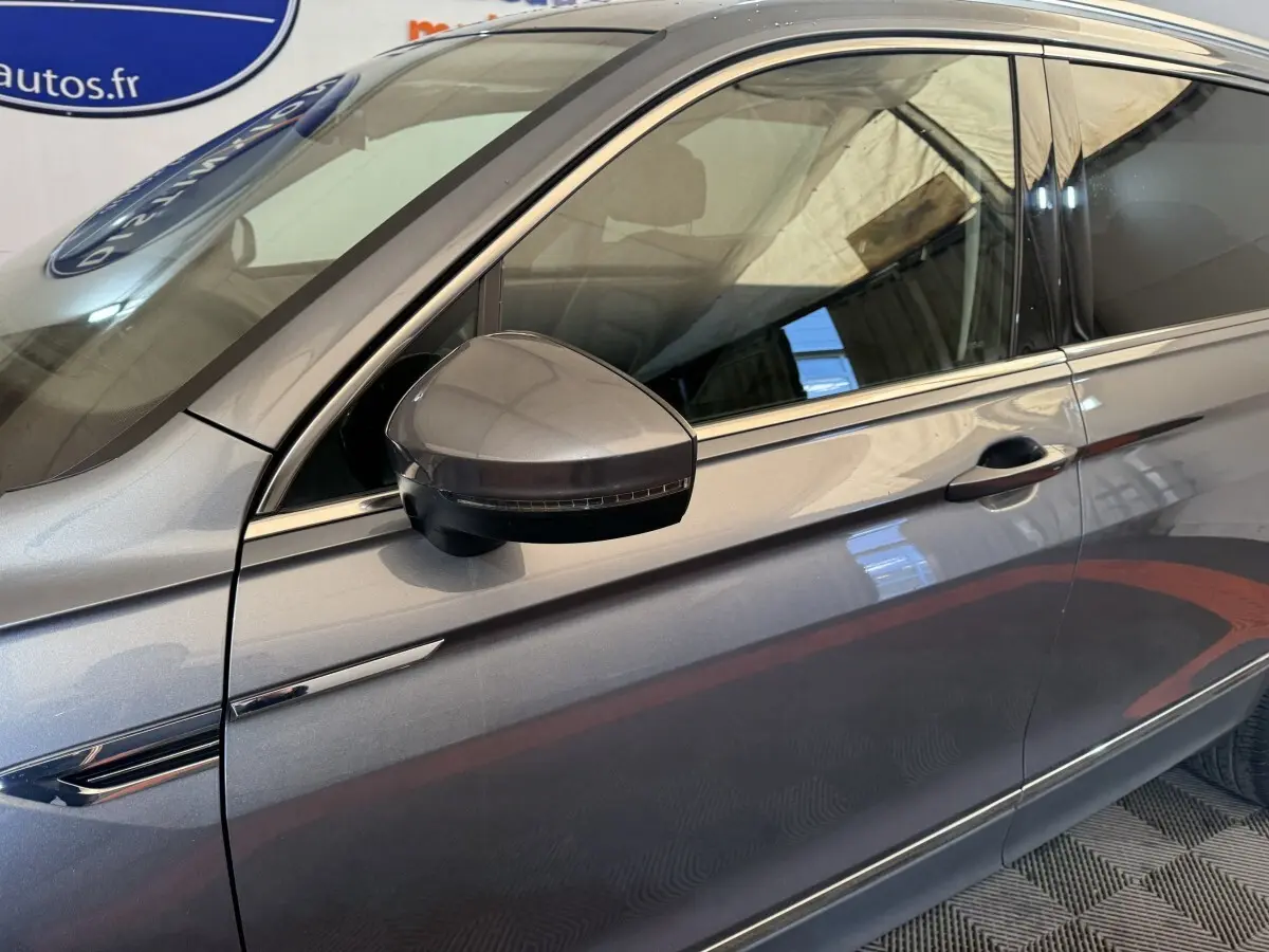 Vue latérale côté gauche du Volkswagen Tiguan Allspace gris foncé, mettant en valeur la ligne de porte et le rétroviseur avec clignotant intégré.
