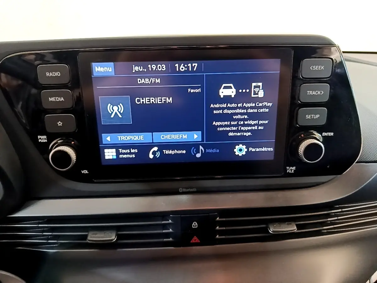 Vue rapprochée de l'écran tactile central noir de la Hyundai i20 2022 affichant la radio et options connectées.