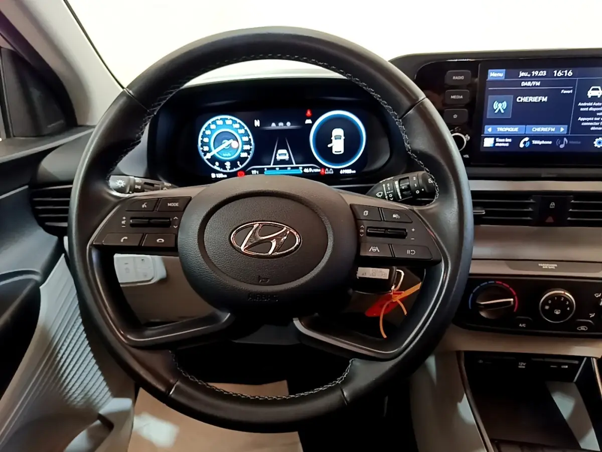 Vue intérieure centrée sur le volant cuir multifonctions et tableau de bord numérique de la Hyundai i20 gris clair 2022.