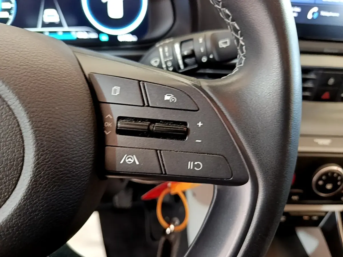 Gros plan sur le volant cuir multifonctions côté gauche de la Hyundai i20 gris clair avec tableau de bord numérique en arrière-plan.