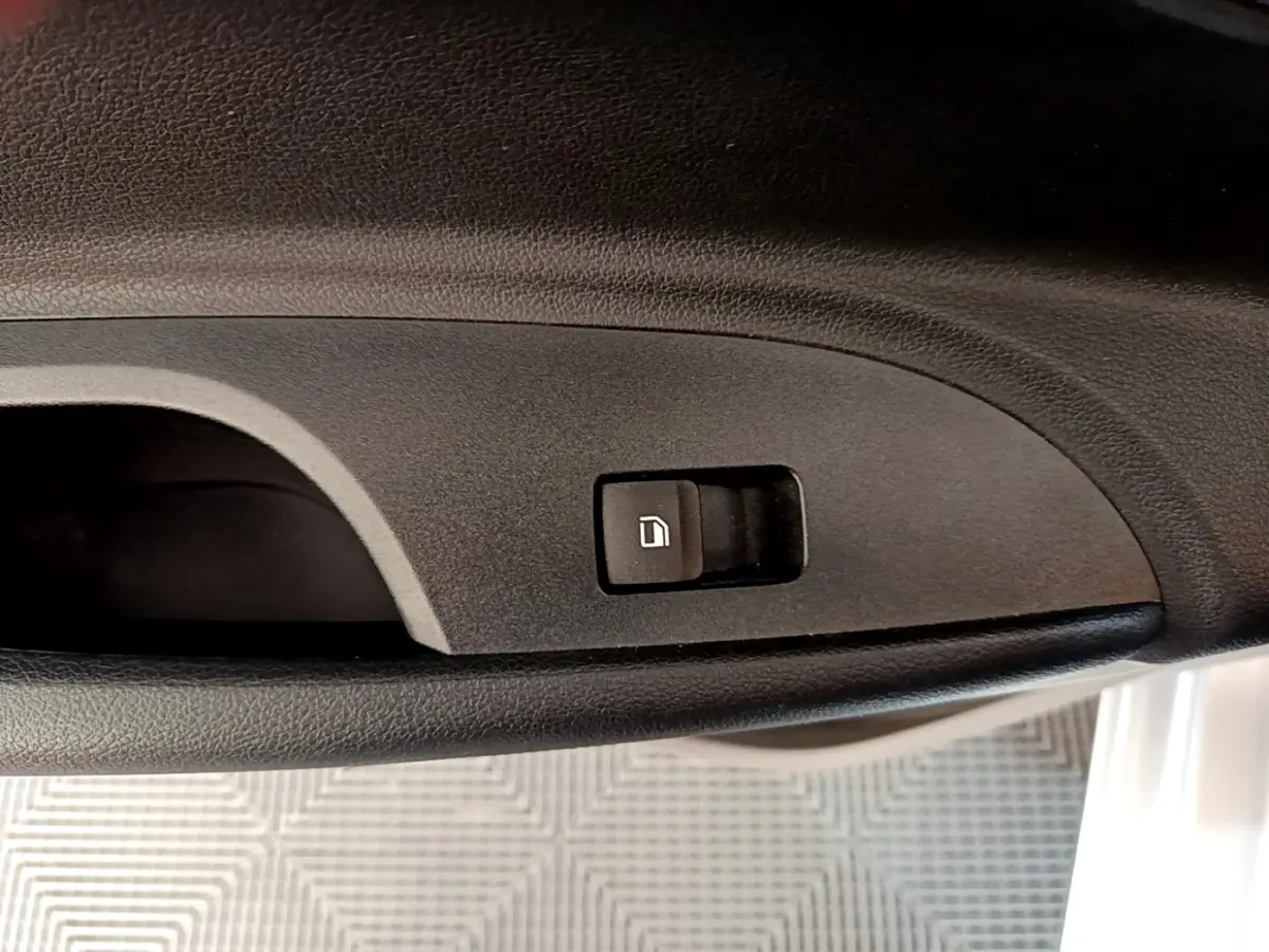 Bouton d'ouverture de coffre intégré dans la garniture intérieure noire côté conducteur de la Hyundai i20 gris clair.