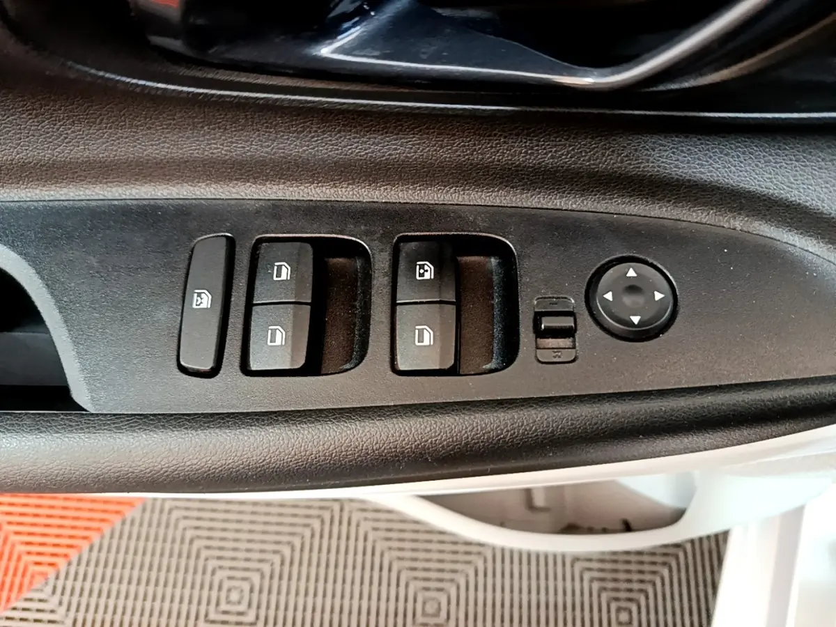 Gros plan sur les commandes de lève-vitres et rétroviseurs côté conducteur d'une Hyundai i20 gris clair 2022.