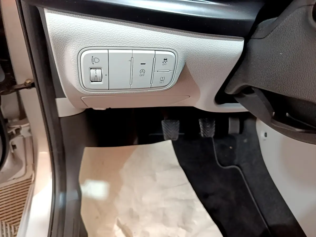 Vue intérieure côté conducteur du tableau de commandes gris clair avec réglage phares et contrôle traction d’une Hyundai i20 2022.