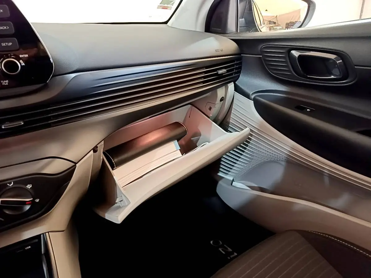 Vue intérieure côté passager de la Hyundai i20 2022 gris clair, boîte à gants ouverte avec documents visibles.