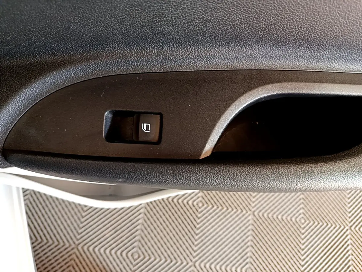 Gros plan sur le bouton de commande de la vitre électrique côté conducteur, intérieur noir texturé.