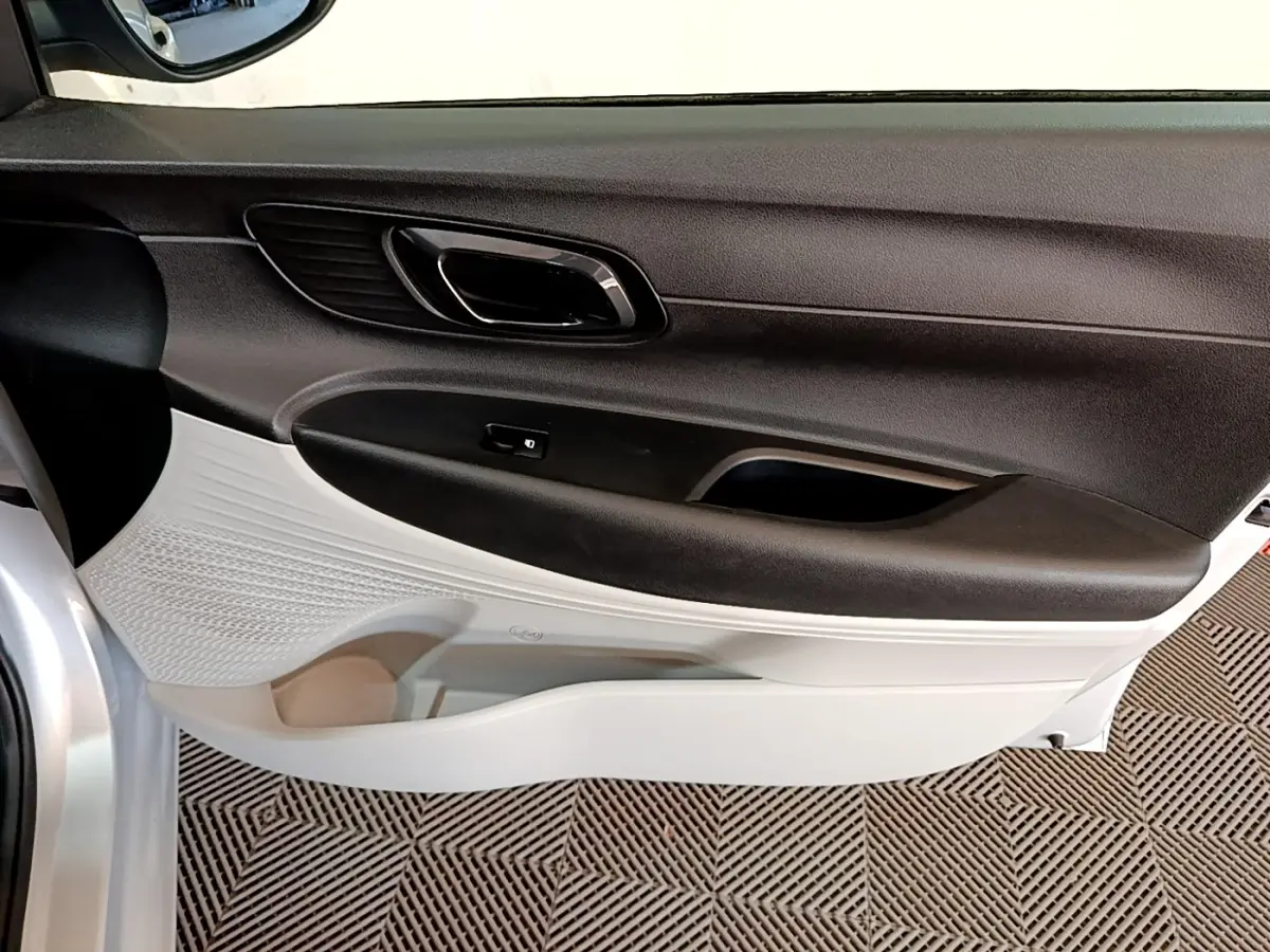 Vue intérieure côté gauche de la porte avant d’une Hyundai i20 gris clair avec poignée noire et panneau bicolore.