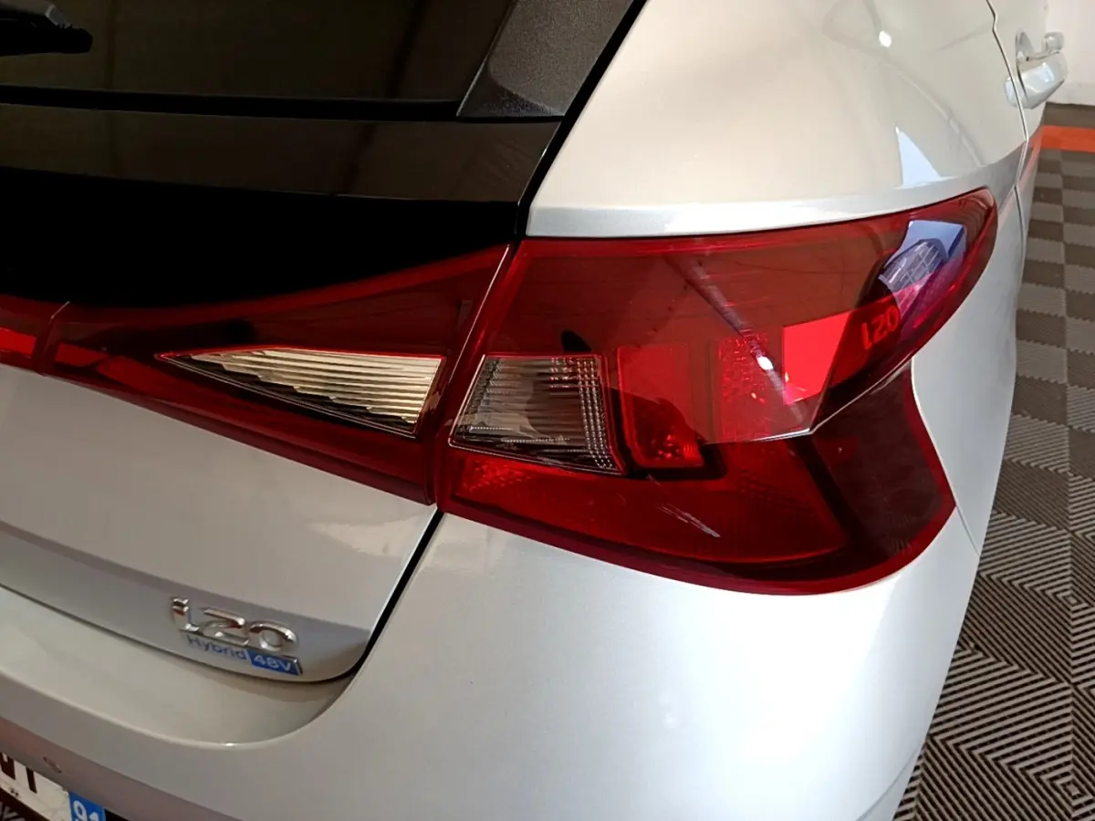 Gros plan sur le feu arrière droit rouge et blanc d’une Hyundai i20 gris clair hybride avec logo i20 visible.