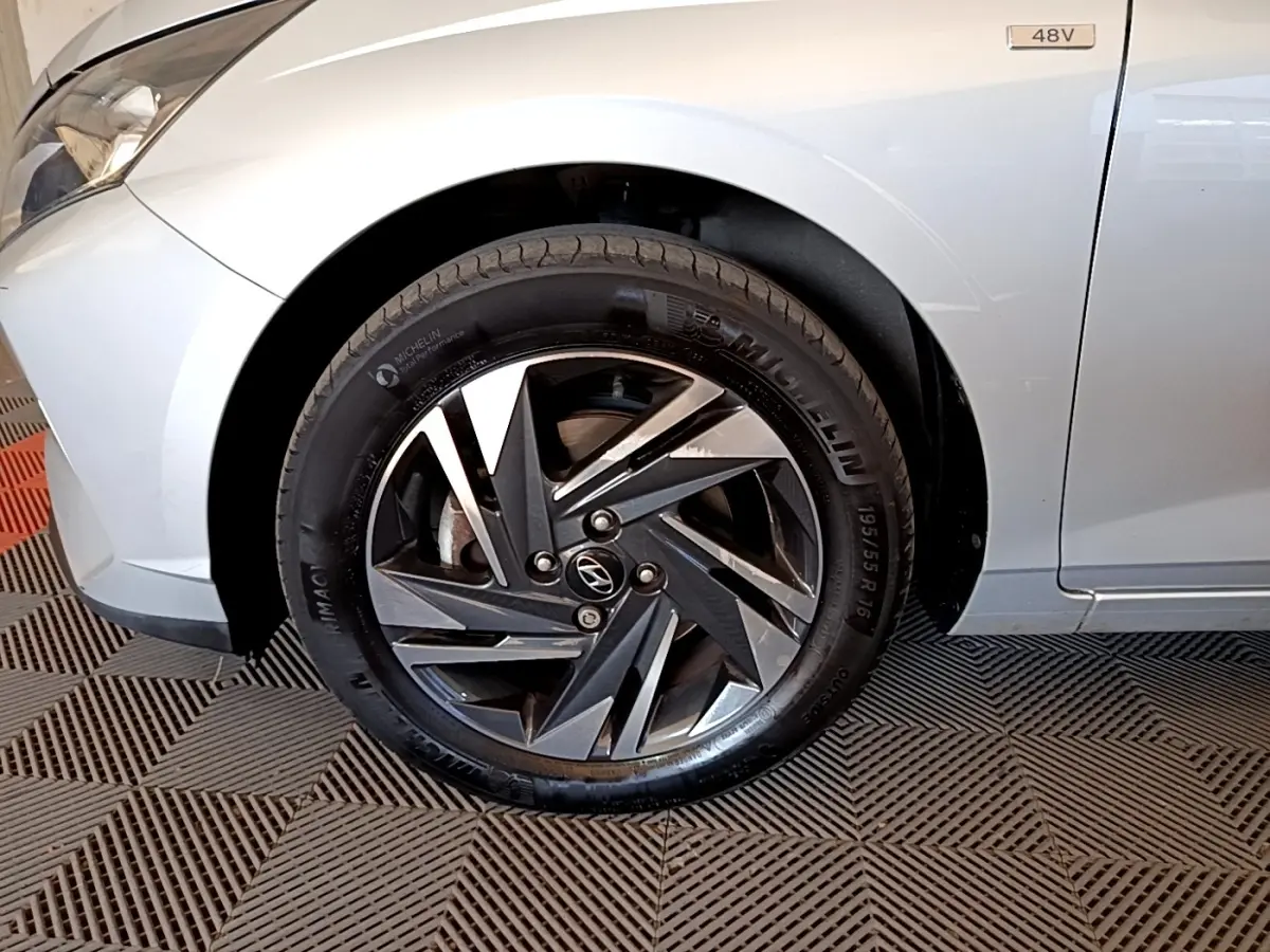 Gros plan sur la roue avant gauche de la Hyundai i20 gris clair avec jante alliage et badge 48V visible sur l'aile.