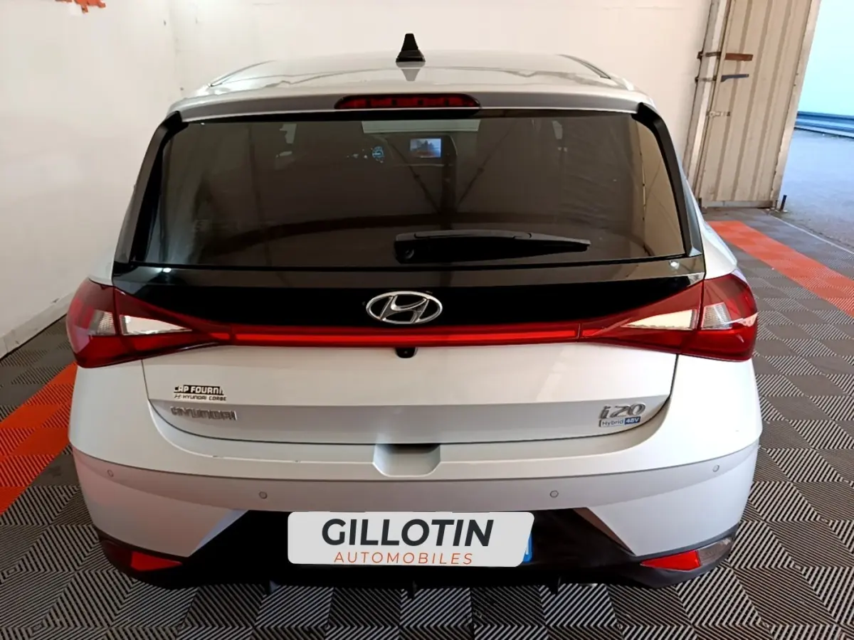 Vue arrière d'une Hyundai i20 gris clair avec feux arrière reliés par une bande lumineuse rouge.