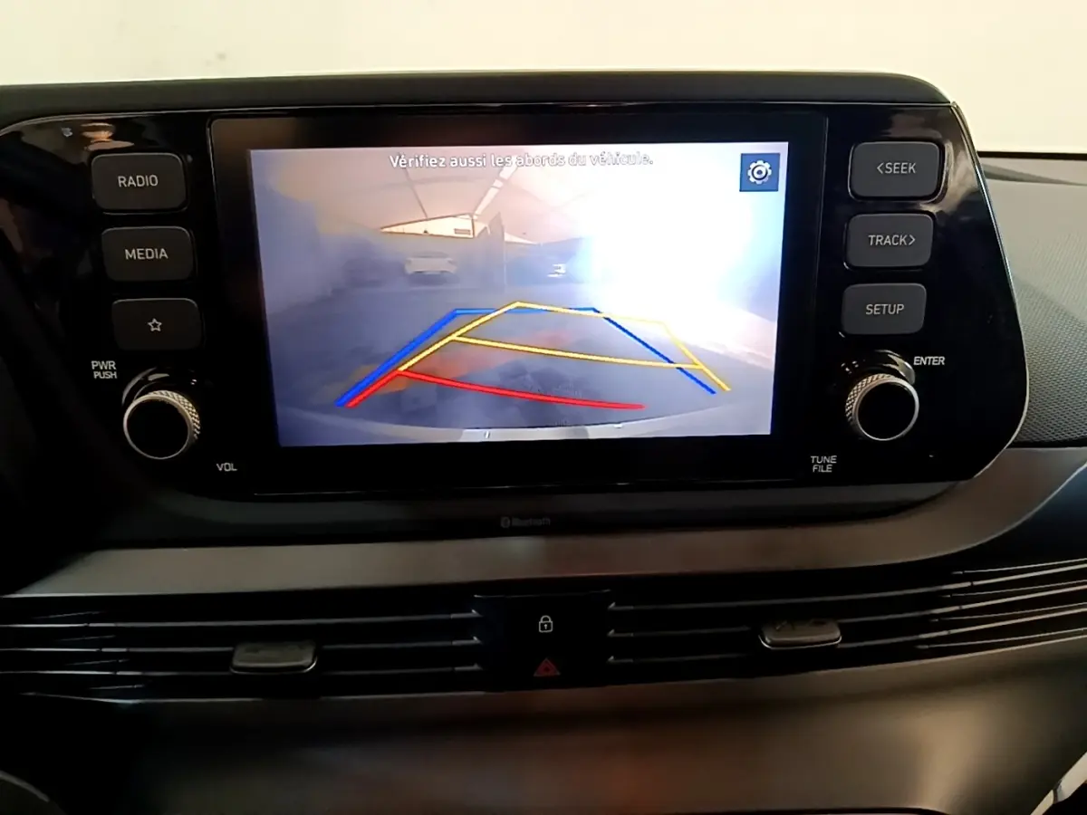 Écran tactile central affichant la caméra de recul avec guidage coloré dans l’habitacle d’une Hyundai i20 gris clair.