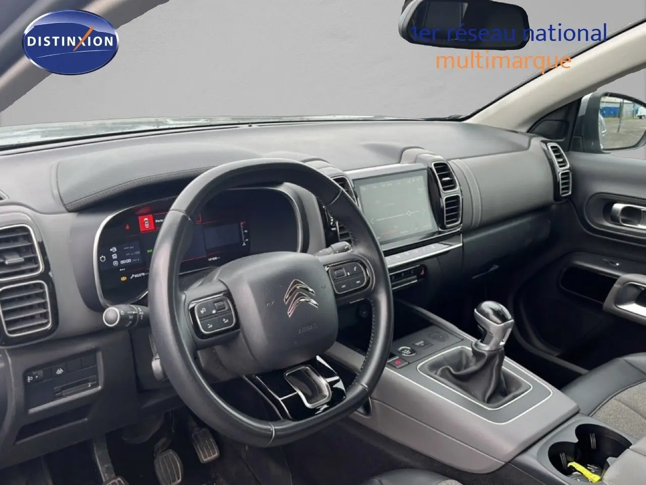 Vue intérieure côté conducteur du Citroën C5 Aircross gris clair, montrant le volant, tableau de bord digital et levier de vitesses manuel.