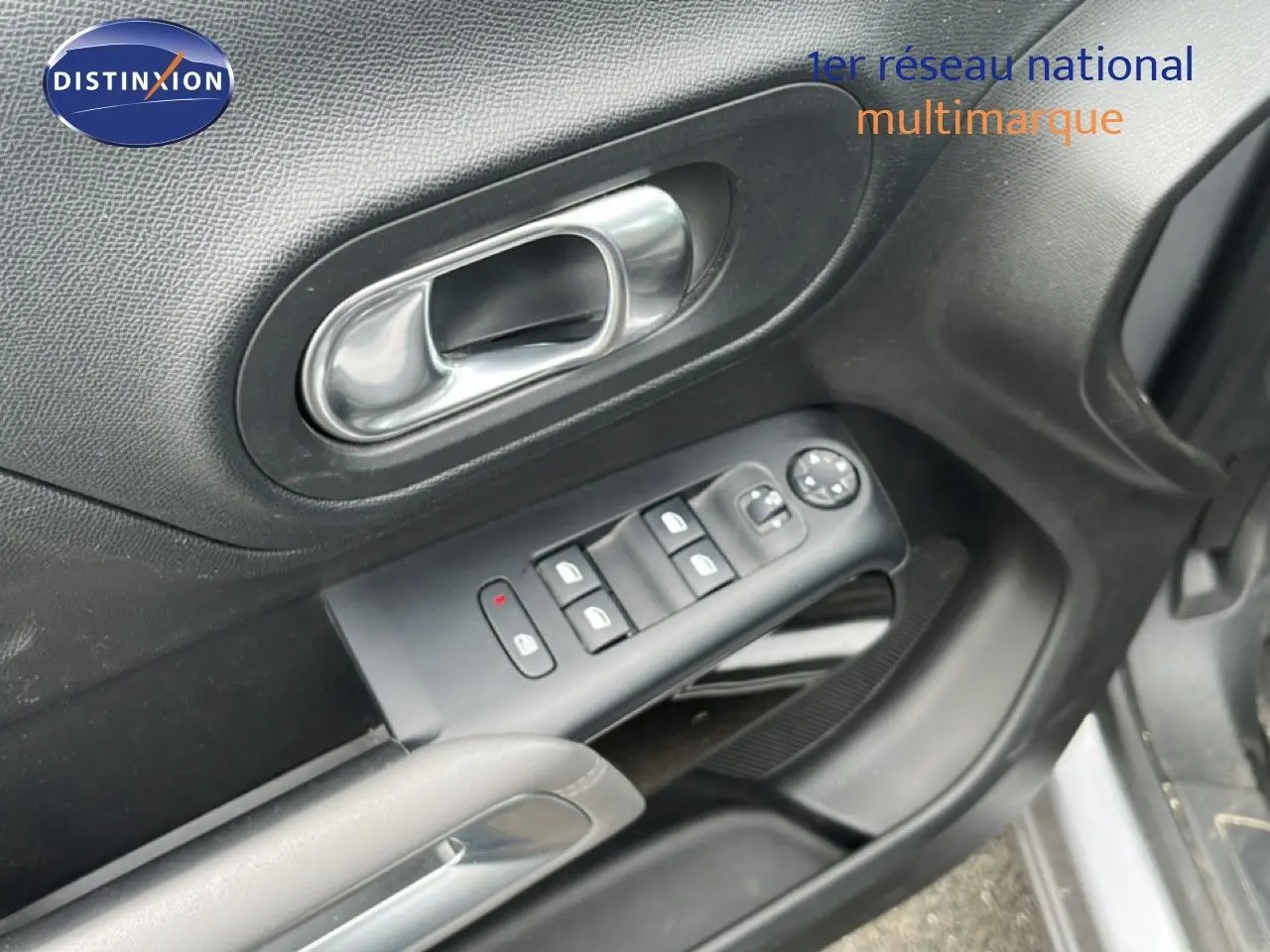 Gros plan sur la porte avant gauche d’un Citroën C5 Aircross gris clair, montrant les commandes des vitres et la poignée intérieure.