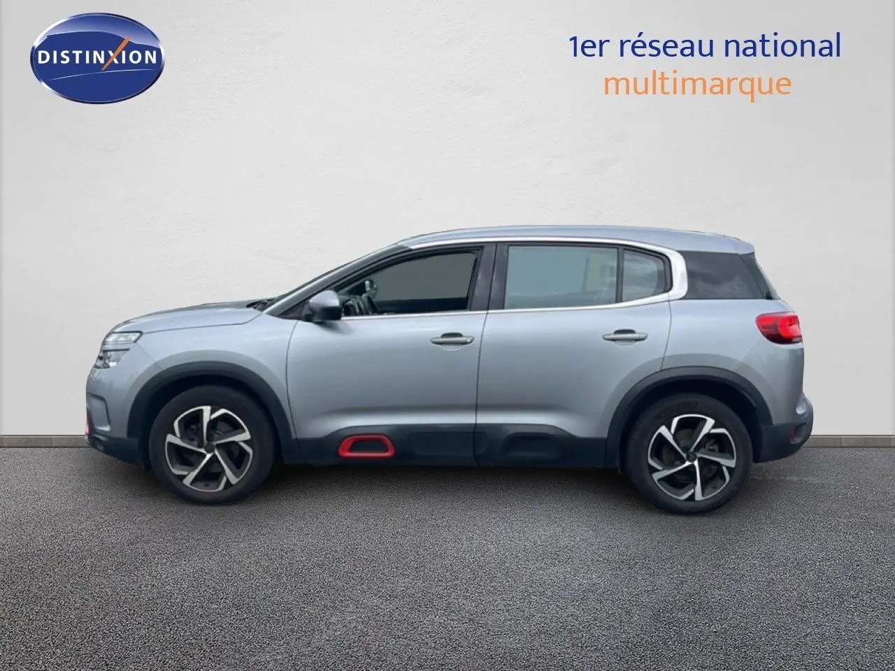 Profil droit d'un Citroën C5 Aircross gris clair métal avec détails rouges sur les bas de caisse et jantes stylisées.