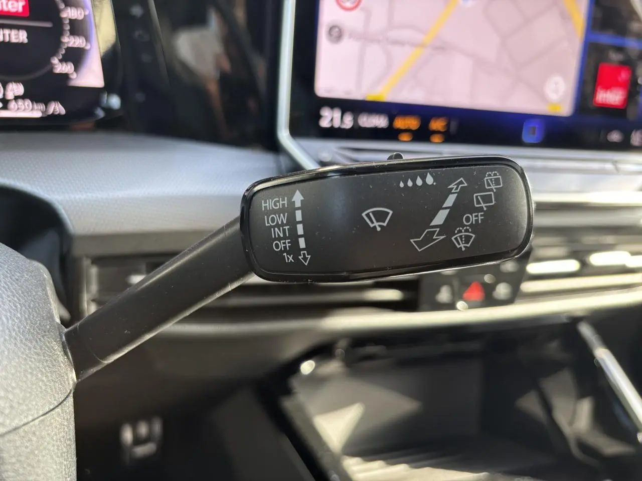 Gros plan sur la commande d’essuie-glace dans l’habitacle de la Volkswagen Golf blanche, avec écran tactile de navigation en arrière-plan.