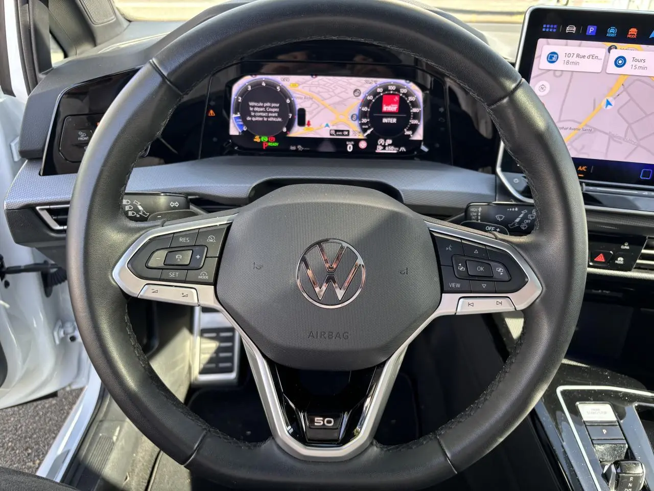 Vue centrée sur le volant noir de la Volkswagen Golf blanc nacré Edition 50 avec tableau de bord digital et écran tactile.