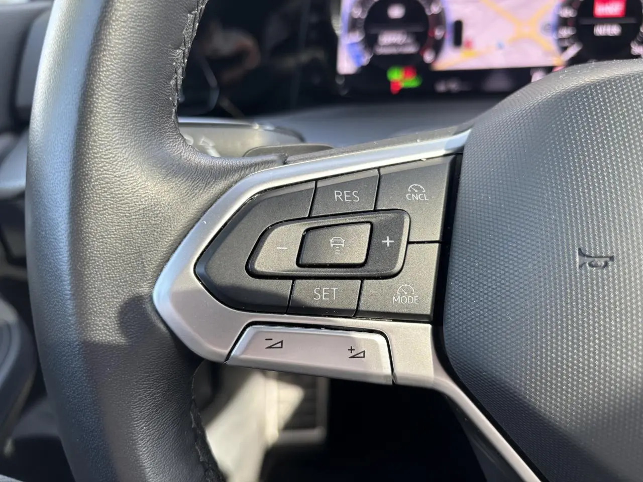 Gros plan sur les commandes au volant à gauche de la Volkswagen Golf 1.5 eTSI blanche, avec affichage digital en arrière-plan.