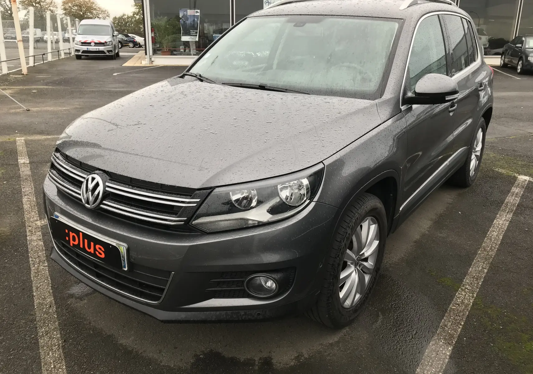 Volkswagen Tiguan Sportline gris foncé vu en 3/4 avant droit sous la pluie, avec jantes alliage et calandre chromée.