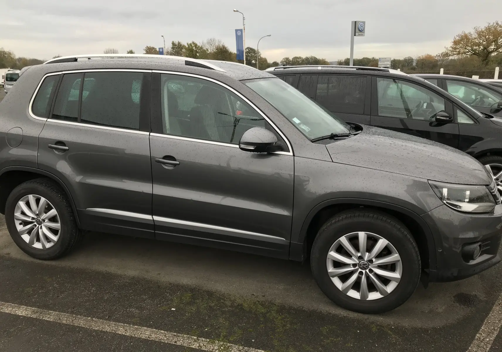 Vue de profil côté gauche d'un Volkswagen Tiguan Sportline gris foncé, avec jantes alliage et toit ouvrant visible.