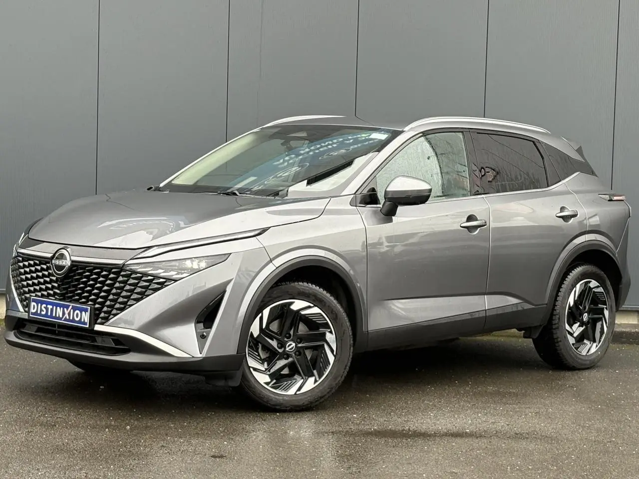 Nissan Qashqai gris Squale en 3/4 avant droit, avec calandre noire texturée et jantes alliage bicolores.