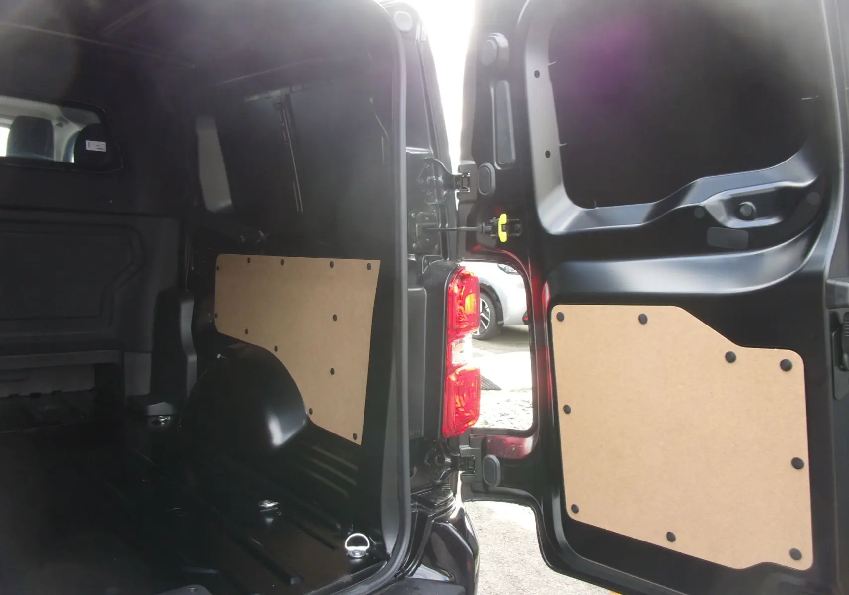 Vue intérieure arrière du Citroën Jumpy Cabine Approfondie noir Perla, portes ouvertes montrant le coffre et panneaux de protection.