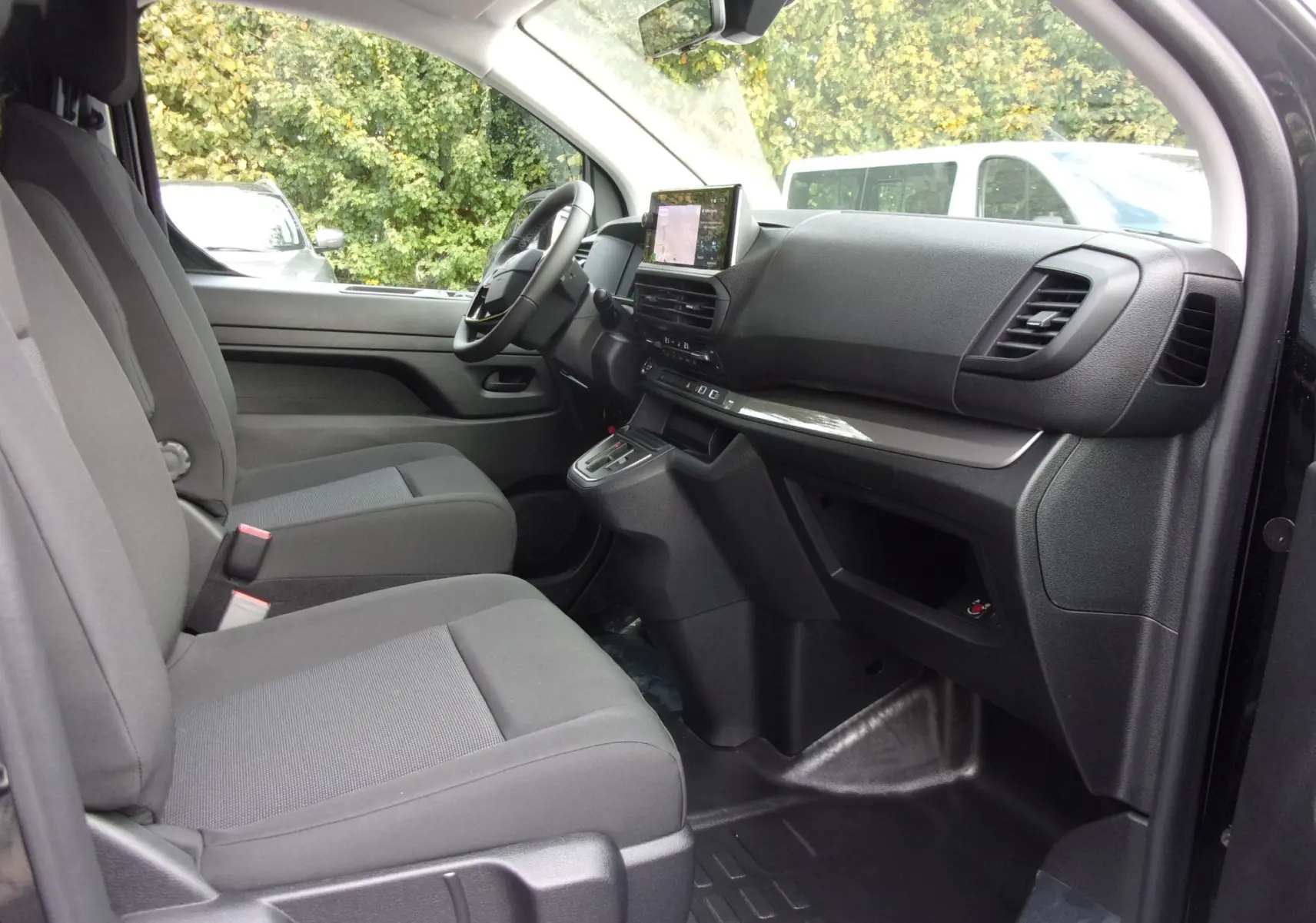 Vue intérieure côté conducteur du Citroën Jumpy XL noir Perla, montrant sièges tissu bi-ton et tableau de bord avec écran tactile.