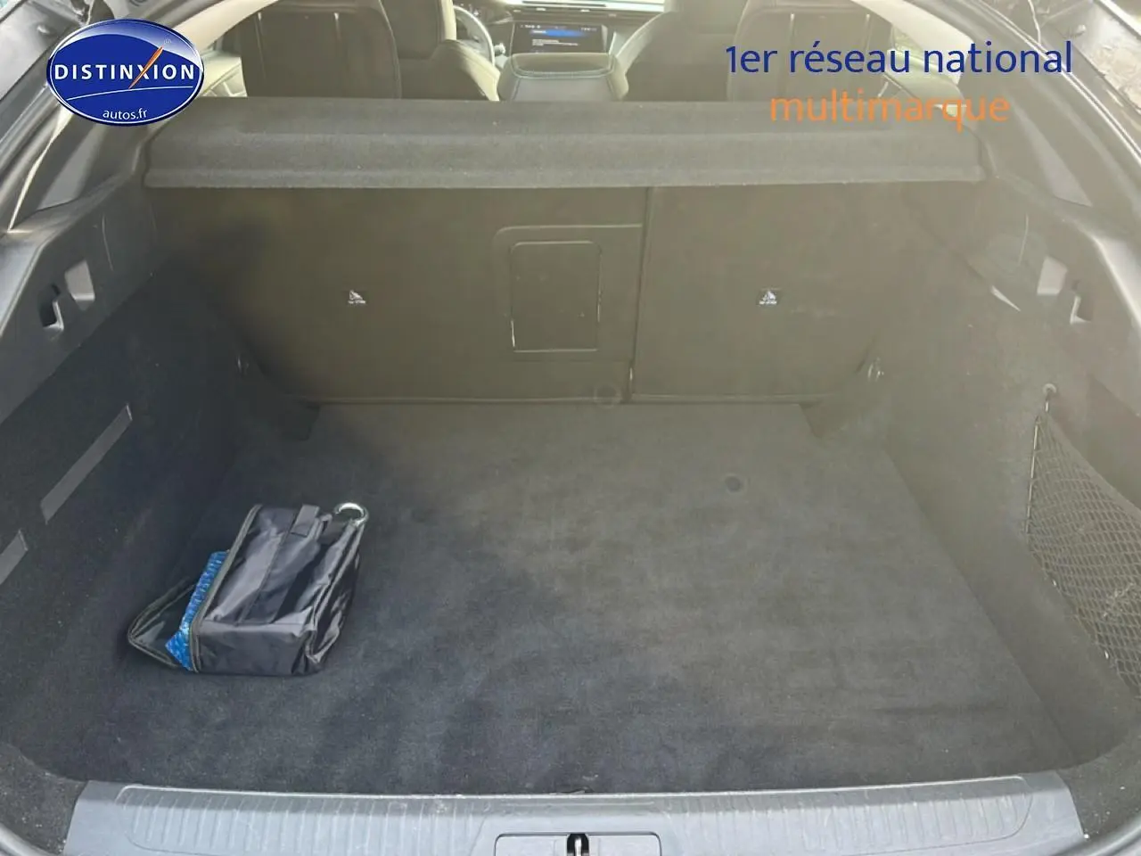 Vue intérieure du coffre spacieux et propre de la Peugeot 408 Hybrid 145 allure gris sélénite avec filet de rangement latéral.