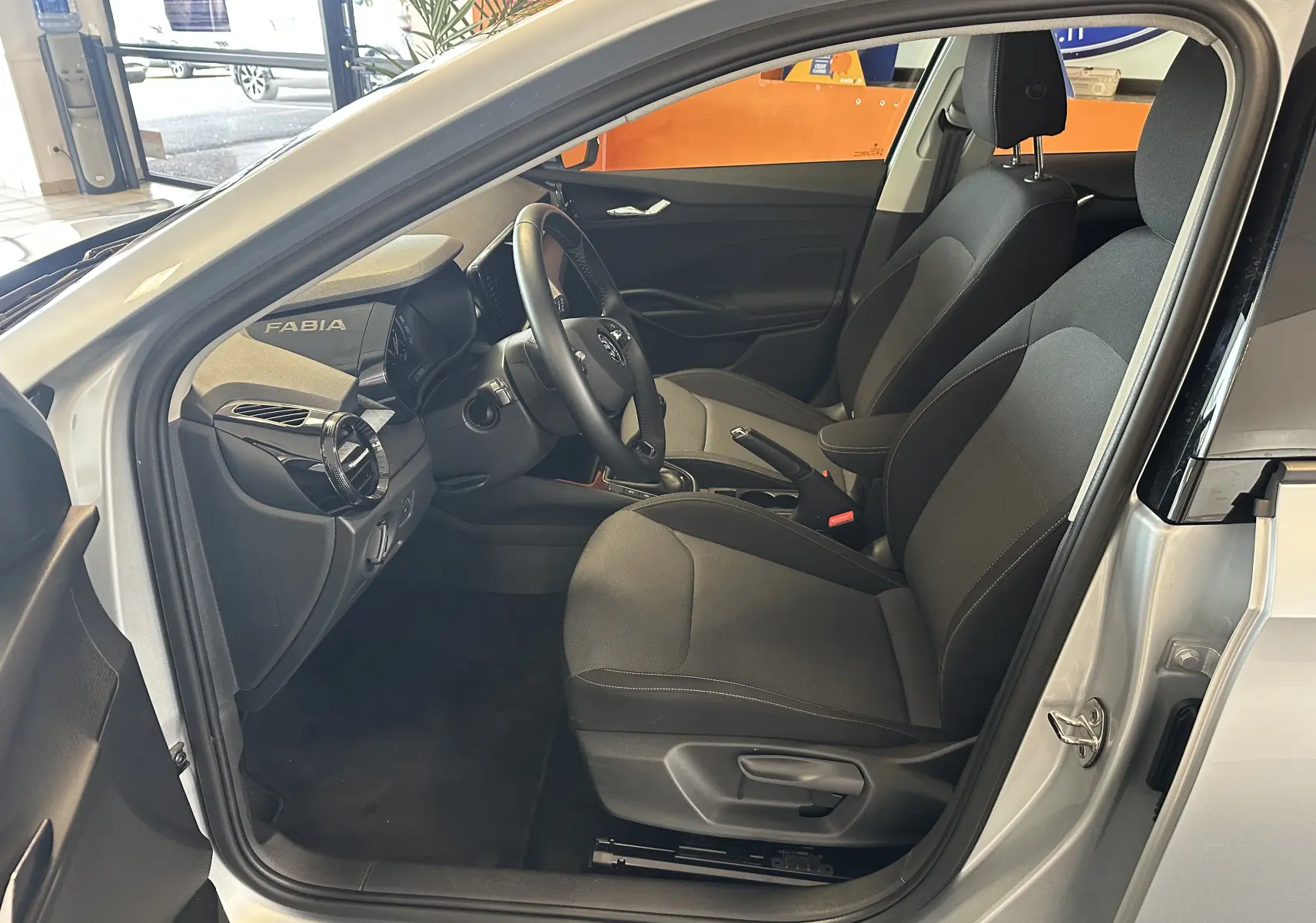 Vue intérieure côté conducteur de la Skoda Fabia Ambition 2023 gris, montrant sièges tissu noirs et tableau de bord moderne.