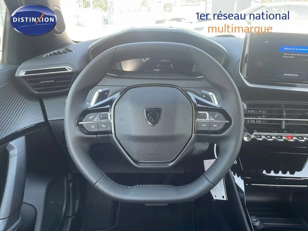 Vue intérieure centrée sur le volant cuir du Peugeot 2008 gris avec commandes au volant et écran tactile visible.