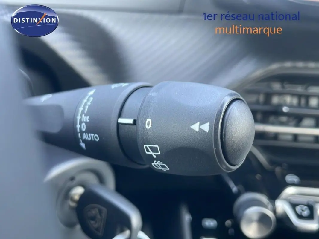 Gros plan sur la commande de l’essuie-glace d’un Peugeot 2008 gris, avec tableau de bord en arrière-plan flou.