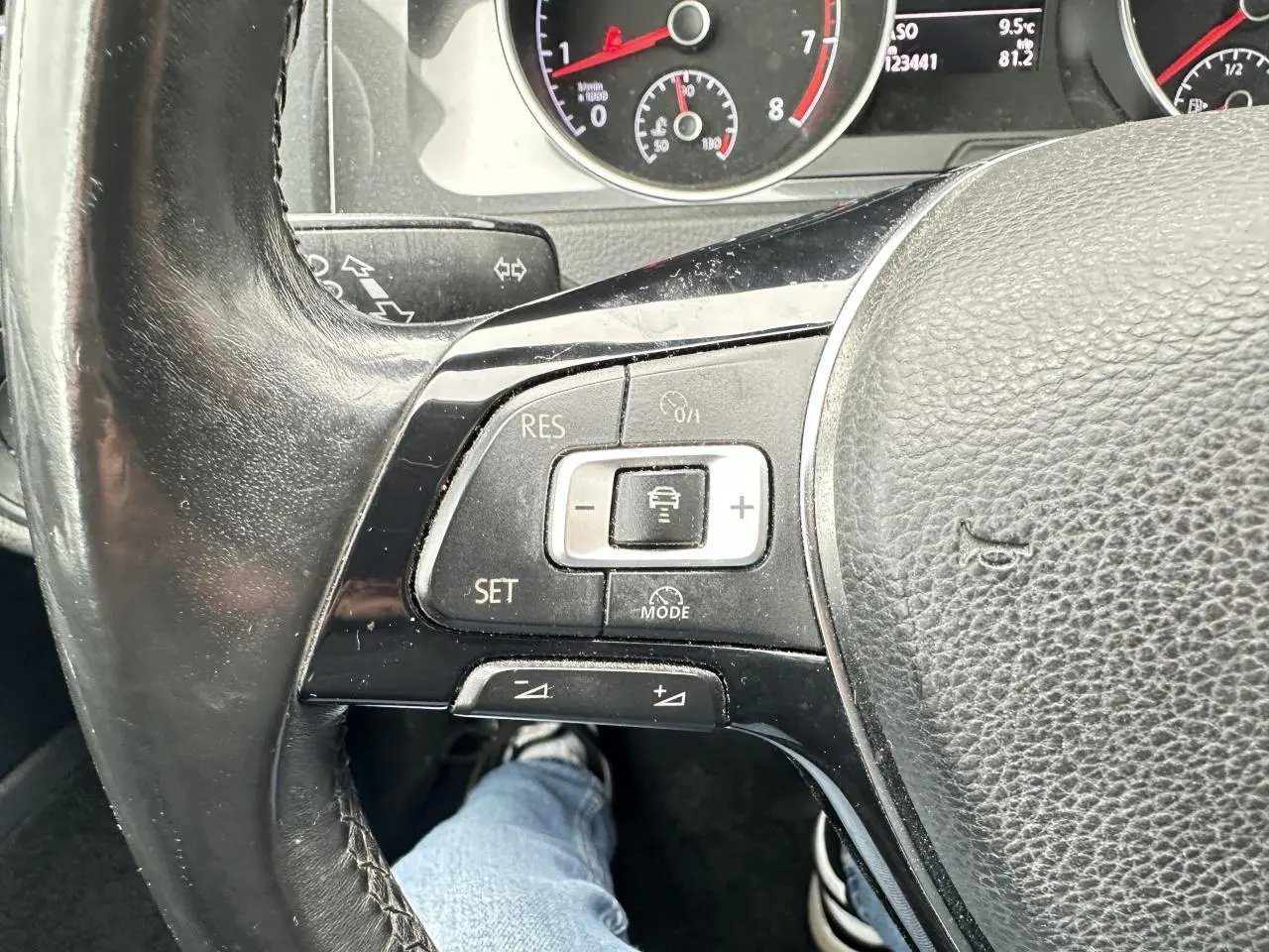 Gros plan sur le volant cuir de la Volkswagen Golf VII gris foncé, avec commandes du régulateur de vitesse et tableau de bord partiel.
