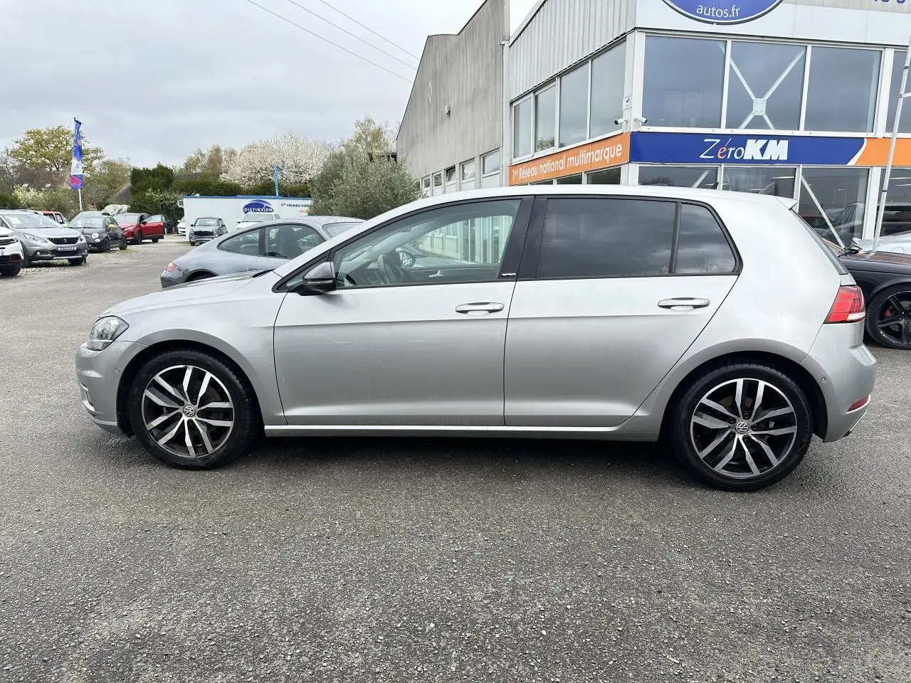 Vue latérale droite d'une Volkswagen Golf VII gris clair avec jantes alliage 17 pouces, vitres arrière surteintées.