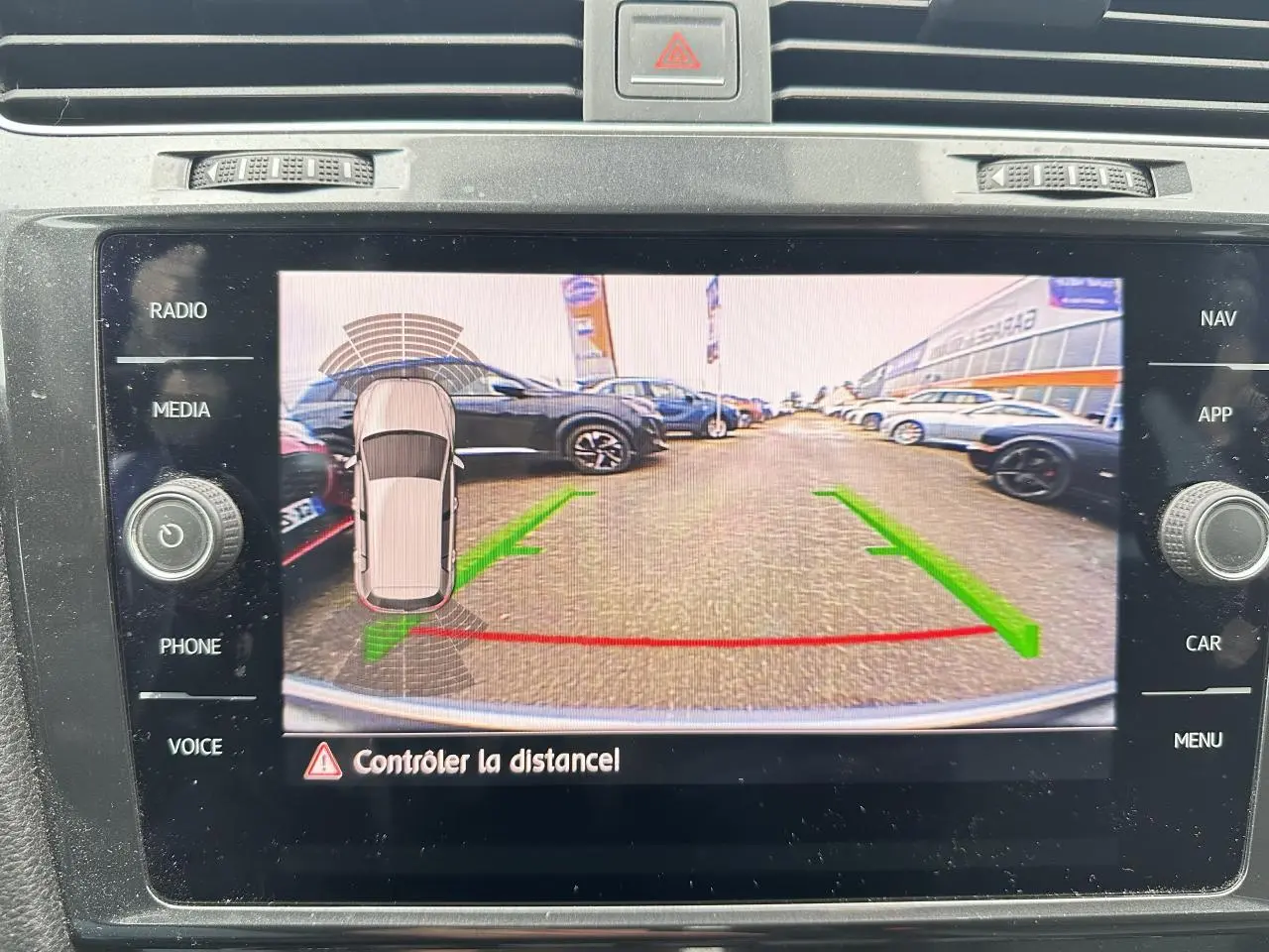 Écran de la radio affichant la caméra de recul d'une Volkswagen Golf gris foncé avec lignes de guidage vertes et rouges.