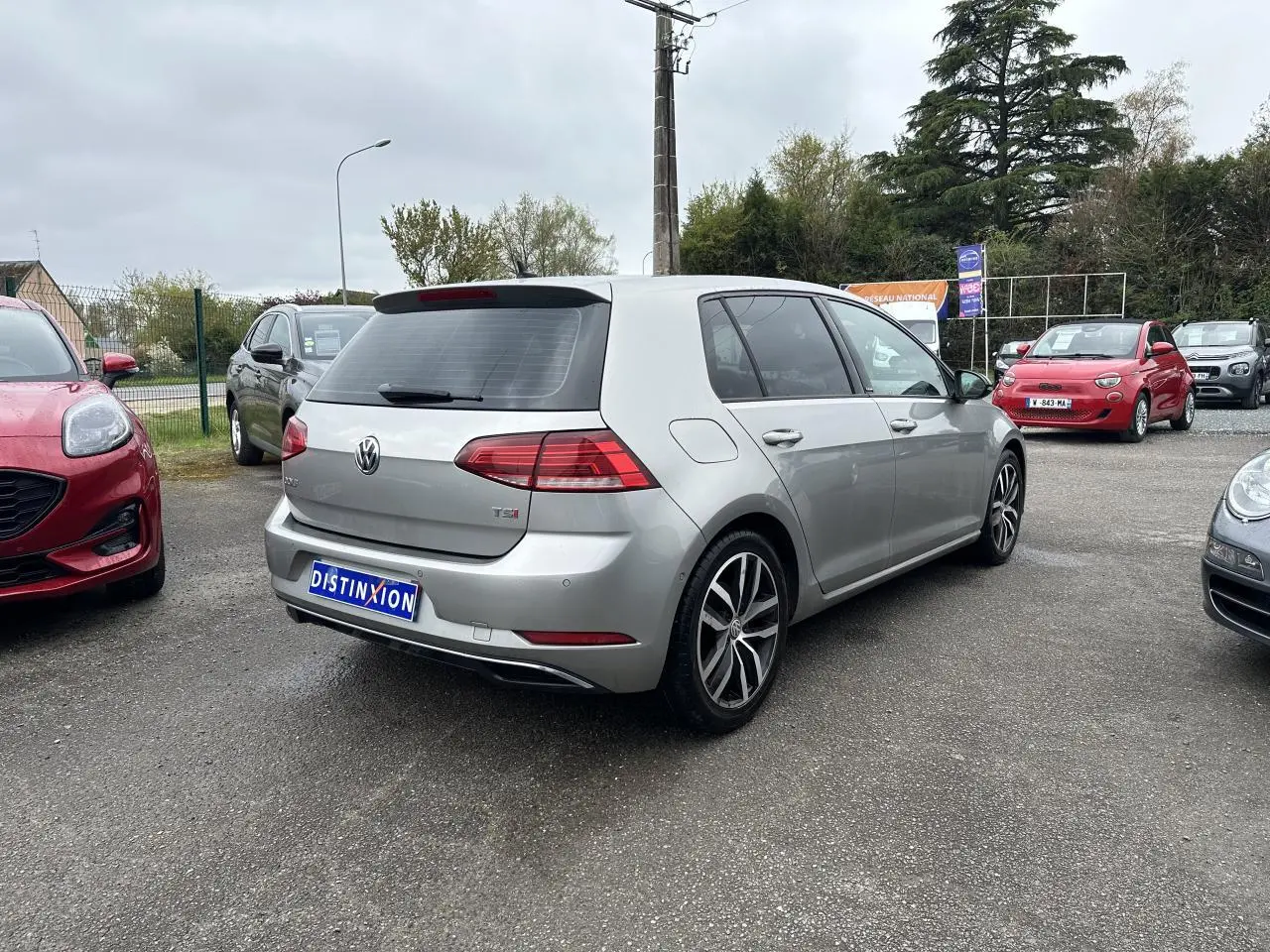 Vue 3/4 arrière droite d'une Volkswagen Golf VII gris clair avec jantes alliage 17 pouces et vitres surteintées.