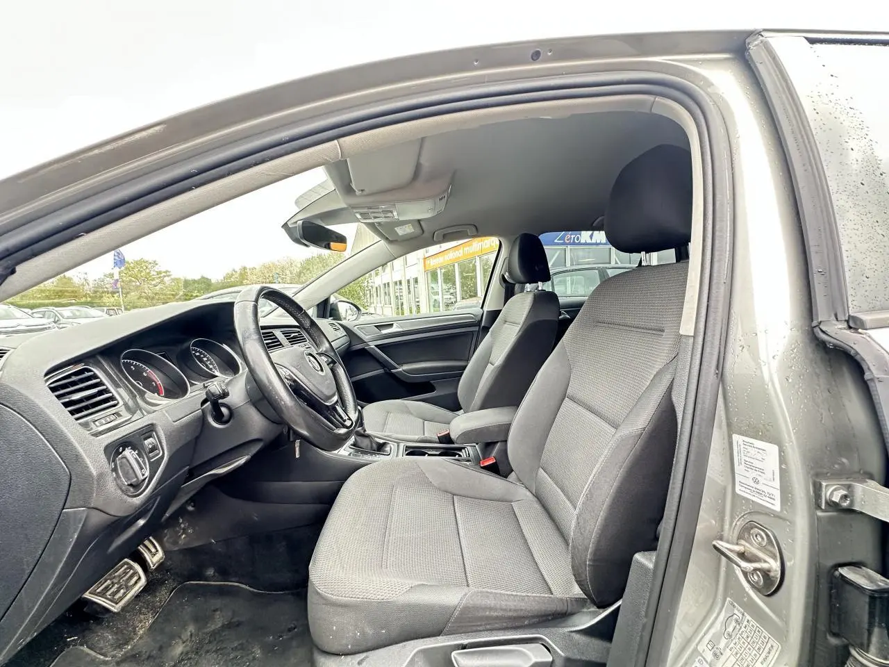 Vue intérieure côté conducteur d'une Volkswagen Golf VII gris foncé, montrant les sièges avant et le tableau de bord.