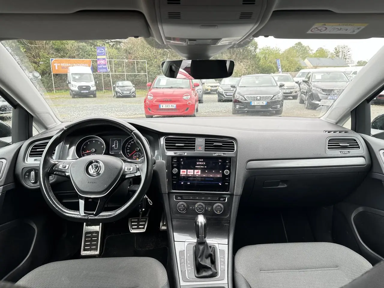 Vue intérieure avant de la Volkswagen Golf VII gris foncé, volant multifonction et écran tactile central allumé.