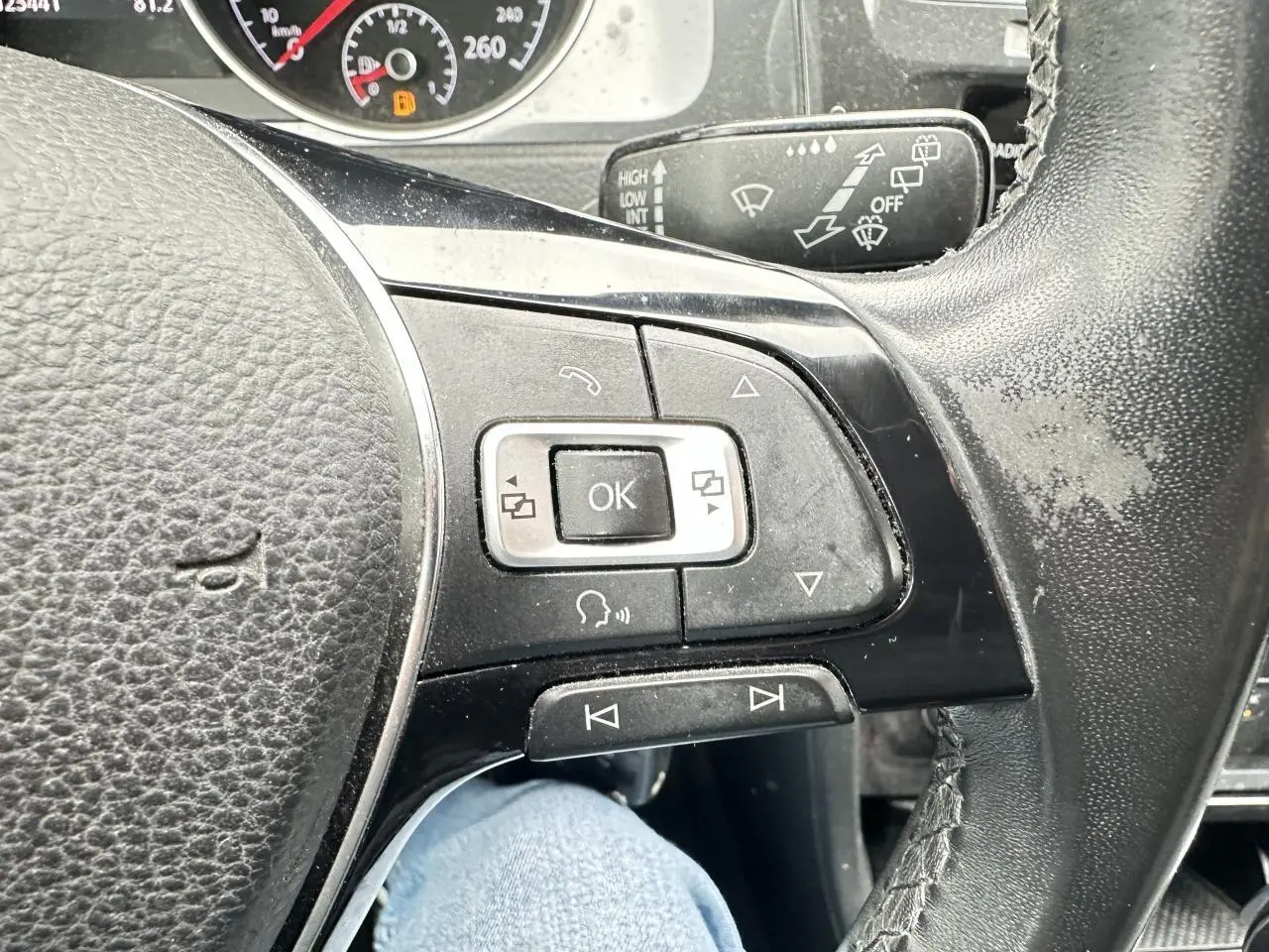 Gros plan sur le volant multifonction en cuir noir de la Volkswagen Golf VII gris foncé, avec commandes intégrées.