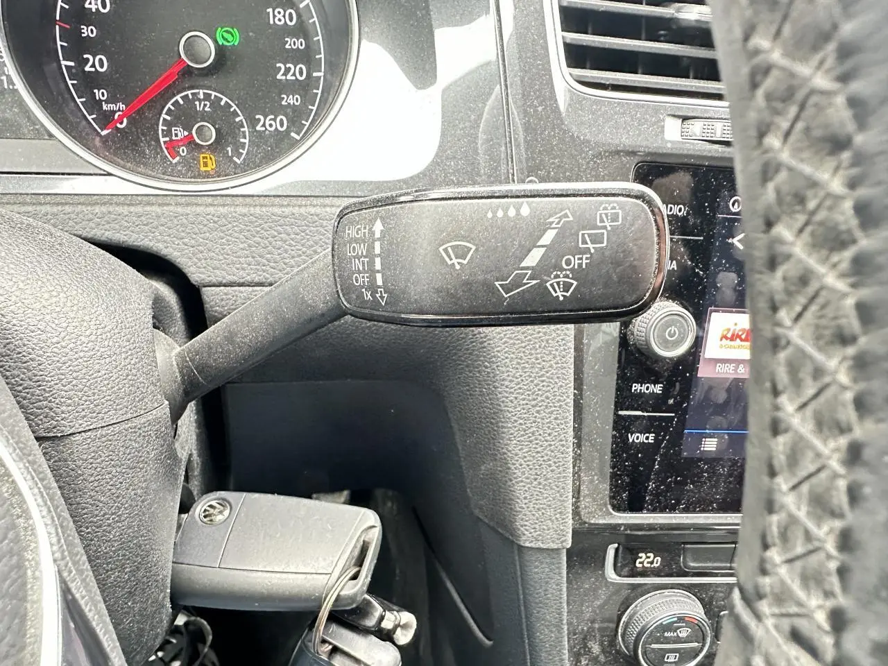 Gros plan sur le commodo d'essuie-glace à gauche du volant d'une Volkswagen Golf VII gris foncé, avec tableau de bord et écran tactile visibles.