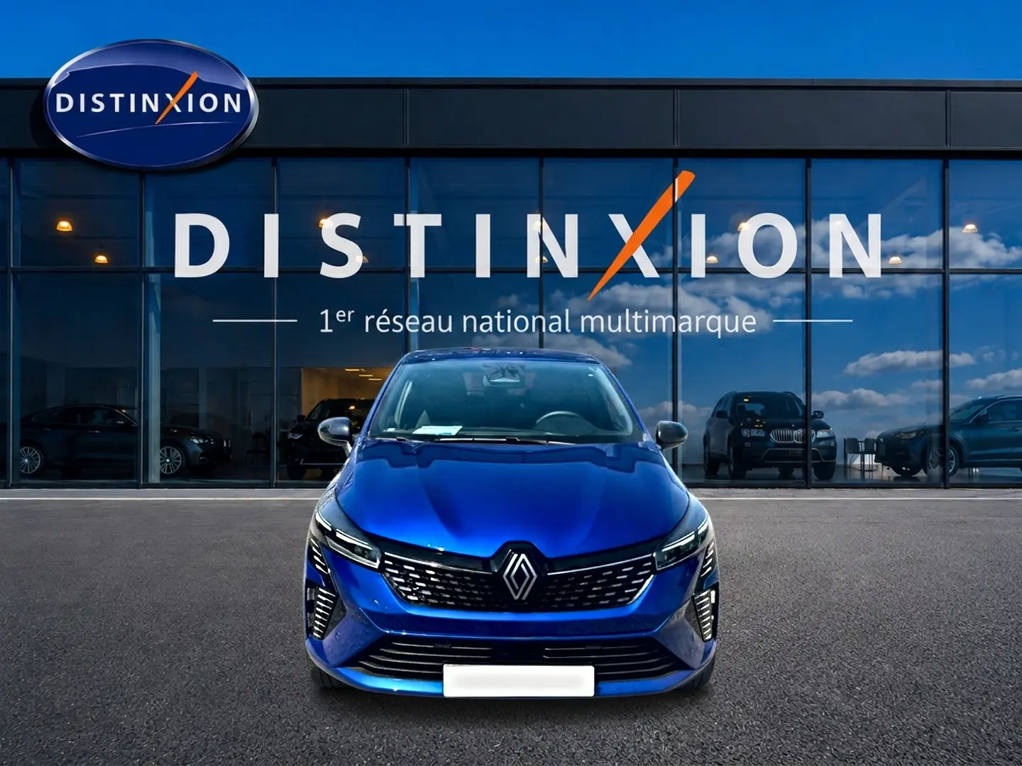 Vue frontale d'une Renault Clio V bleu iron garée devant une vitrine avec logo Distinxion.