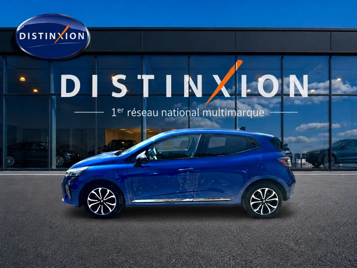 Profil côté gauche d'une Renault Clio V 1.0 TCe 90 Techno bleu iron avec jantes alu devant une vitrine Distinxion.